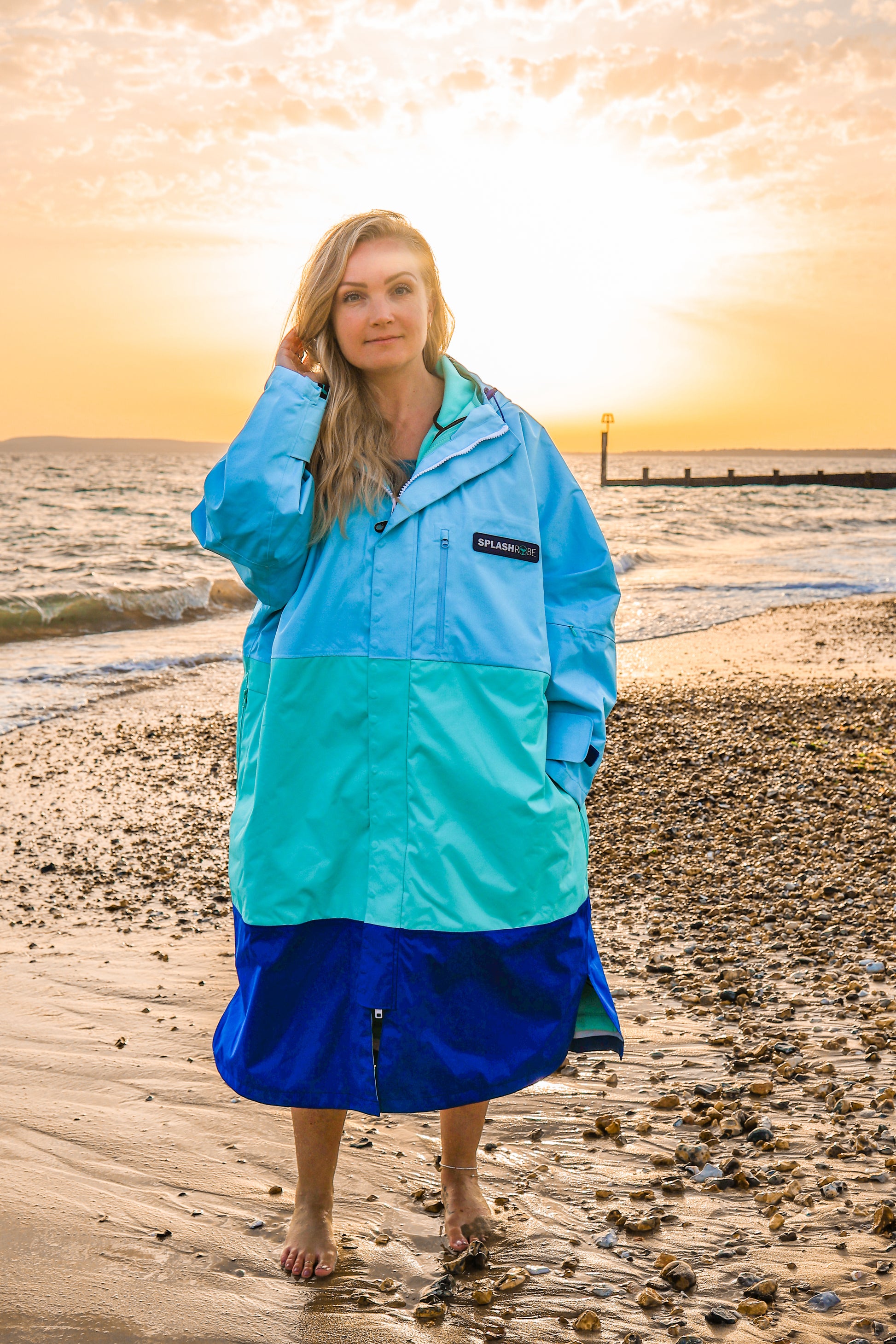 Female wearing the 3 way splashrobe with the sun setting behind her on a beach