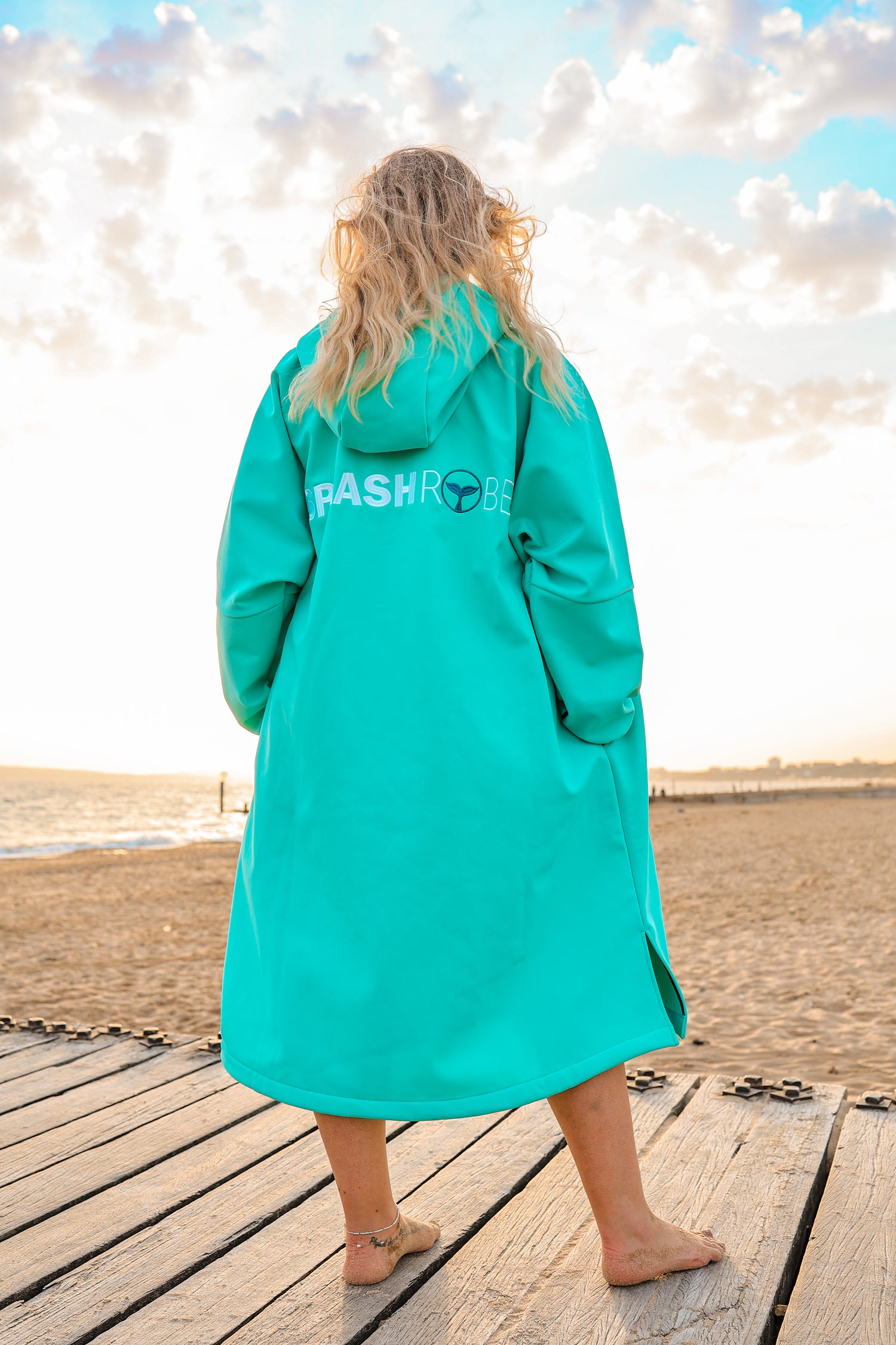 Woman standing on beach wearing SplashRobe inner coat. Back view