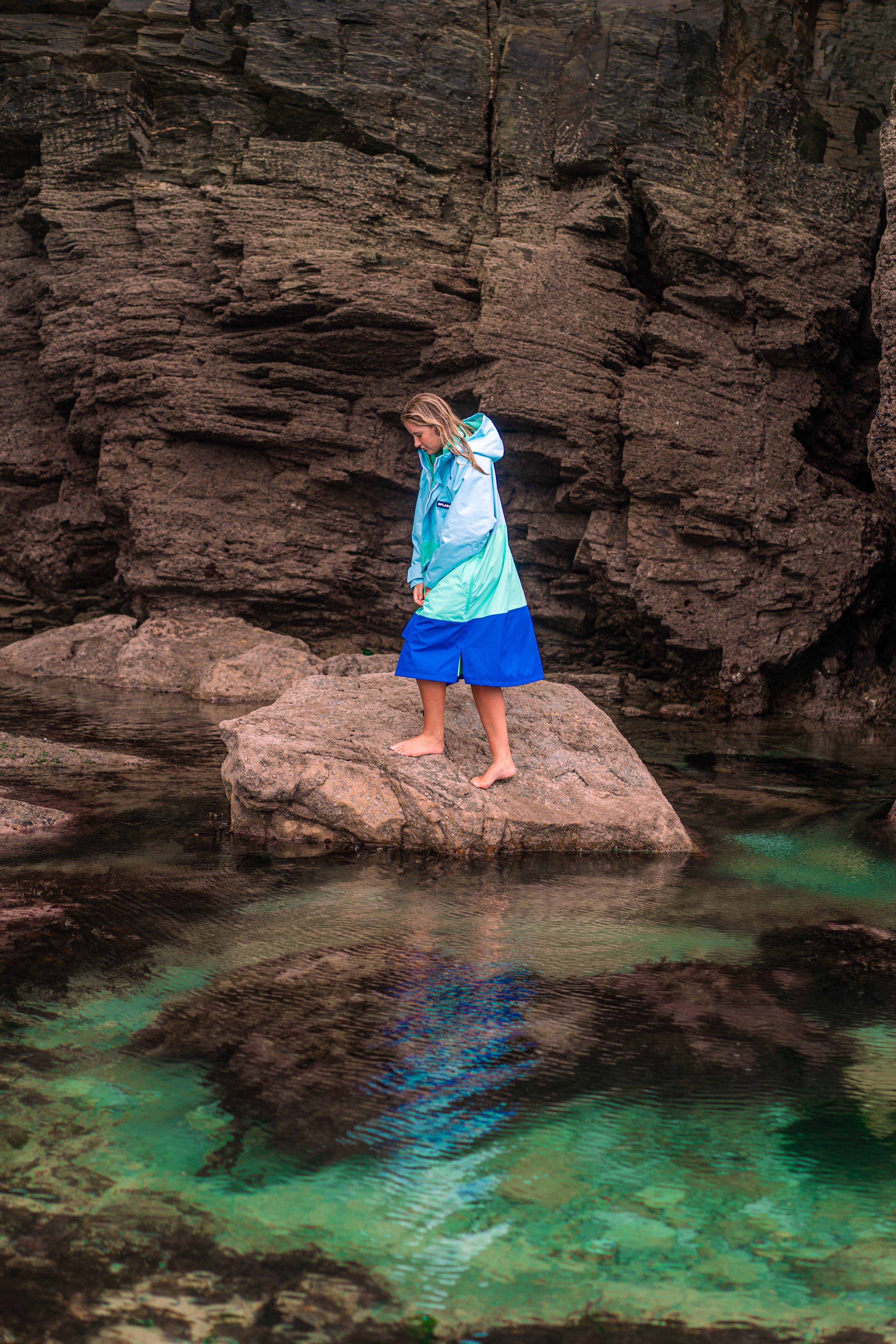 Woman walking across rock pools at the bottom of a cliff in the 3 way SplashRobe